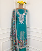 Teal dress with intricate white embroidery on a mannequin against a white wall.
